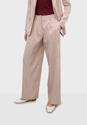 Pantaloni a gamba larga con righe verticali rosse e bianche, abbinati a un blazer coordinato e scarpe bianche con punta affilata.