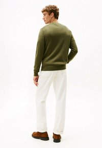 Maglione lavorato a maglia verde con scollo a V, abbinato a pantaloni bianchi e scarpe in suede marroni. Il maglione presenta polsini e orlo a coste.