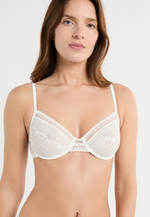 Soutien-gorge en dentelle blanche avec motif floral, panneaux en tulle transparent, bretelles réglables et finition douce et texturée. Structure à armatures pour un maintien optimal.