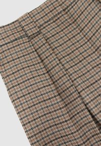 Tessuto a quadretti marrone e nero con motivo a spina di pesce con cuciture visibili su una sezione di indumento piegato.