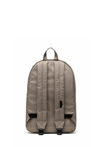 Sac à dos en tissu beige de forme arrondie, avec deux bretelles, une poignée supérieure et des accents noirs. Texture lisse avec des détails de couture rembourrés.