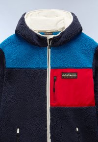 Fleece jacket featuring a blue upper, dark navy sleeves, and a red chest pocket. Zipper closure with pull tab and logo detail on pocket.