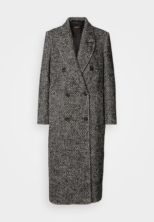 Dobbeltbrystet frakke i sort og hvidt herringbone mønster med reverskrave, to frontlommer og sorte knapper.
