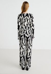 Combinaison à motifs noir et blanc avec une coupe décontractée, des manches longues et une texture plissée, dotée d'un design à jambes larges et d'un col rond.