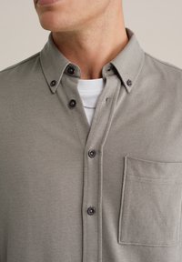 Grijs overhemd met knopen, gemaakt van een gestructureerde stof, voorzien van een kraag en een borstzak. Zwarte knopen creëren een contrast met het patroon van het materiaal.