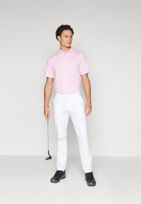 Pink striped polo shirt with a collar, paired with white trousers and black golf shoes. A golf club is held in the left hand.