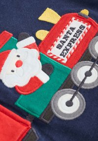 Röd och grön broderad tomte på ett tågmotiv med vita hjul, mot en mörkblå texturerad tygbakgrund.