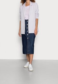 Ljuslila kavaj över en ljuslila topp, ihop med en mörkblå denimkjol med framknappar och vita sneakers.