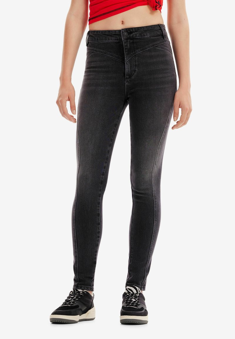 Gros plan d'une personne portant un jean skinny noir taille haute, un crop top rouge, des baskets noires et des chaussettes à motif zèbre, debout.