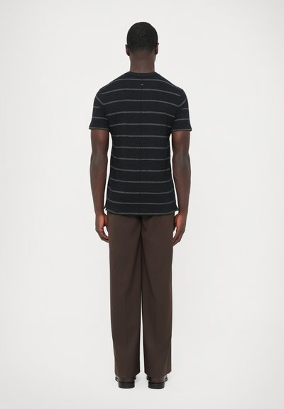 Schwarzes T-Shirt mit kurzen Ärmeln und Streifen, gerade geschnitten, kombiniert mit lockeren braunen Hosen. Glatte Stoffstruktur, minimalistisches Design, keine sichtbaren Markenkennzeichnungen.