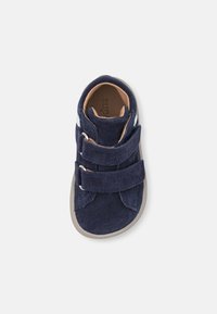 Scarpa alta in suede blu navy con due cinturini regolabili in Velcro e suola in gomma grigia chiara. Presenta un morbido rivestimento interno.