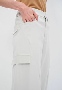 Lichtgrijze cargobroek met een gladde textuur, voorzien van een voorkoopsak en een extra zijzak met klep, ritssluiting.