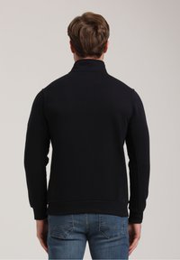 Dunkelblauer Pullover mit hohem Kragen, langen Ärmeln, gerippten Bündchen und Saum. Glatte Textur mit minimalen Nähten.