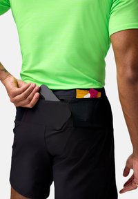 Svarta sportshorts med en elastisk midja; en grön tröja. En telefon läggs i bakfickan tillsammans med energibarer.