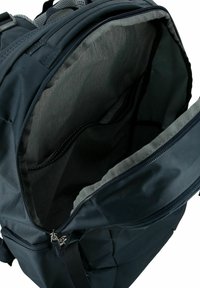 Mochila negra con una apertura con cremallera, con un interior gris, forro texturizado y un bolsillo lateral. Se pueden ver las correas ajustables.