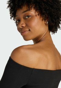 Czarna bluzka bez ramiączek z prążkowaną teksturą, zestawiona z małymi złotymi i srebrnymi kolczykami, eksponująca naturalny odcień skóry i kręcone włosy.