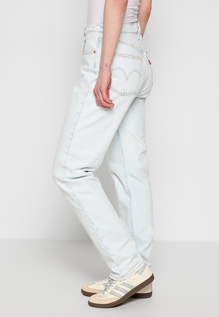 Vaqueros de mezclilla azul claro, de talle alto y diseño de pierna recta. Cuentan con bolsillos traseros con costura en forma de arco. Llevados con zapatillas beige.