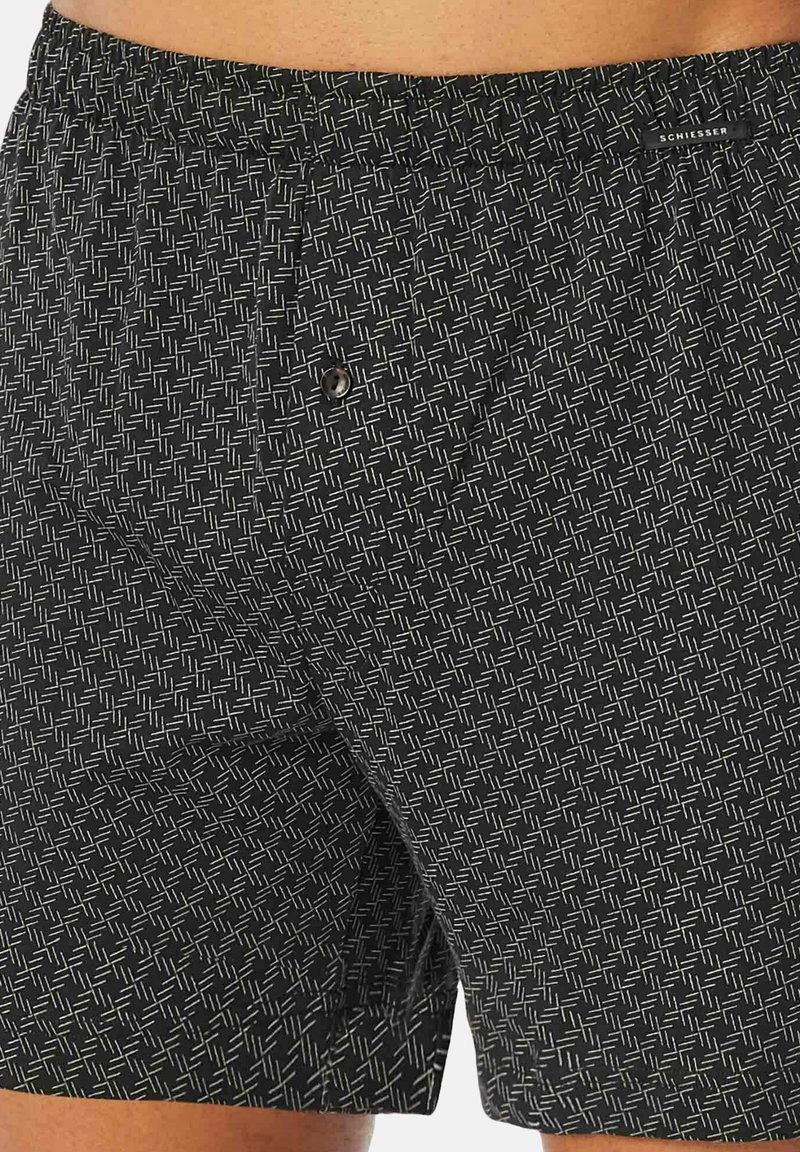 Zwarte zwemboxers met een textuurpatroon van witte geometrische vormen, elastische tailleband en een knoopdetail aan de voorkant. Lichtgewicht, sneldrogend materiaal.