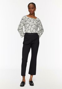 Chemise à manches longues à motif floral blanc associée à un pantalon noir ajusté et des mocassins noirs brillants, présentant une coupe slim et un détail discret à la taille.