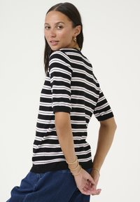 Chemise en tricot rayée noir et blanc à manches courtes, coupe décontractée et poignets côtelés. Les accents notables incluent une légère texture et des couleurs contrastantes.