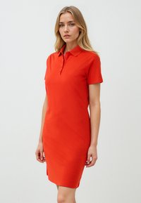 Rode polokleed van zachte katoen met een kraag, korte mouwen en een rechte pasvorm, met een zijsplit voor bewegingsvrijheid.