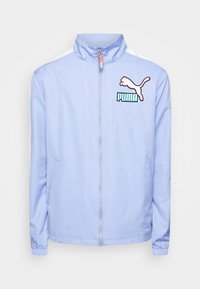 Lyseblå jakke lavet af glat stof med høj krave, frontlynlås, sidelommer og et Puma-logo i kontrasterende farver.