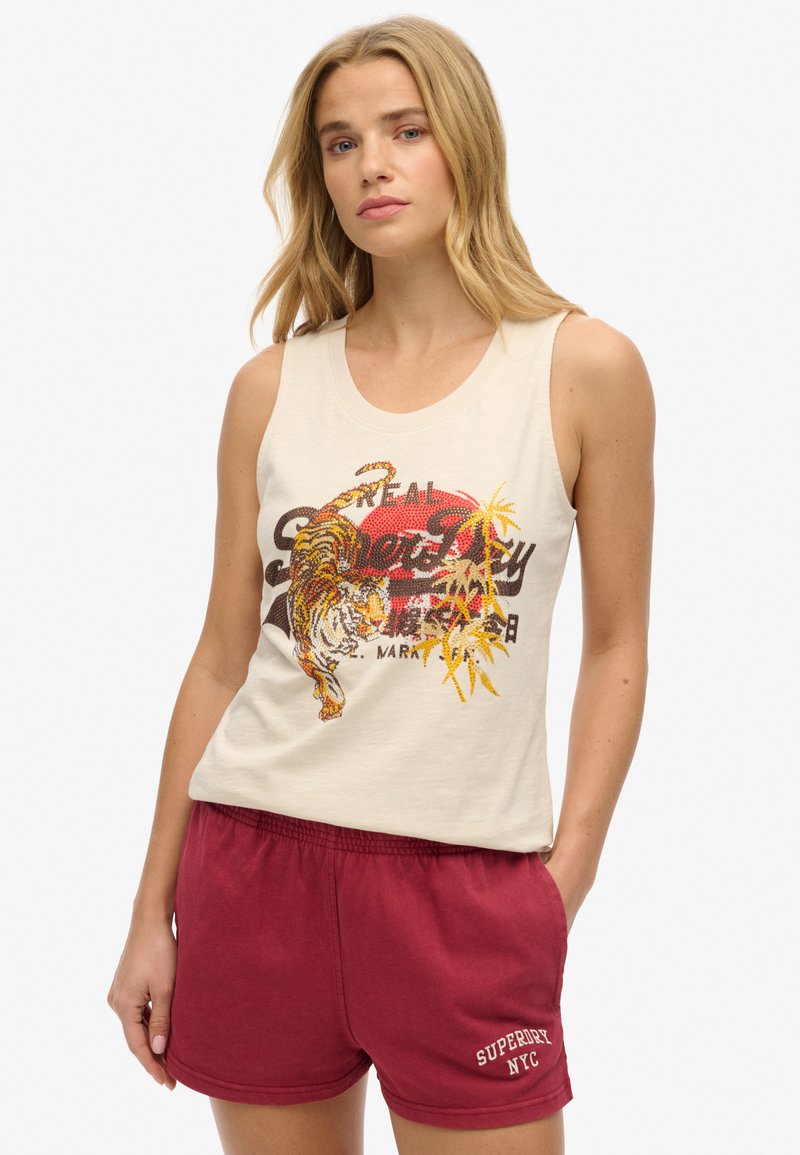 Débardeur beige clair avec un graphique de tigre et des accents tropicaux ; associé à un short en coton bordeaux portant le texte blanc "Superdry NYC".