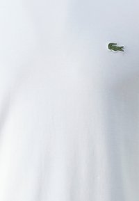 T-shirt en coton blanc avec un petit logo de crocodile brodé en vert sur le côté supérieur gauche. Texture douce et col rond classique.