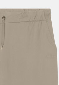 Pantalones ligeros beige fabricados con una tela suave, que cuentan con una cinturilla elástica, cordón de ajuste y un sutil logo en relieve en el lateral.