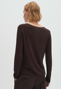 Braunes langärmeliges Oberteil mit weiter Ausschnitt und eng anliegenden Ärmeln. Glatte Textur, minimales Design und dezente Rückendetail am Saum.