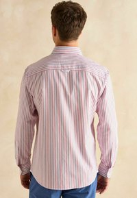 Pánska košeľa s dlhým rukávom biela s červenými a modrými vertikálnymi pruhmi. Má ktorú zapínanie na gombíky a jednoduché gombíkové manžety.
