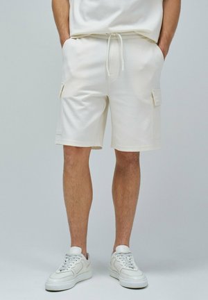 Shorts de algodón blancos con bolsillos cargo laterales, cintura con cordón y un corte relajado, combinados con zapatillas blancas.