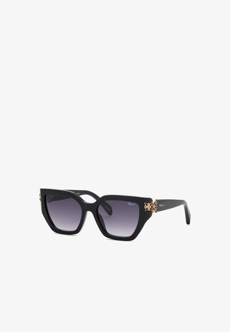 Lunettes de soleil noires œil de chat avec verres foncés dégradés et accents floraux dorés sur les branches.