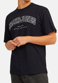 Black cotton t-shirt featuring white text "JACK & JONES" and "EST.90 WORLDWIDE" in bold font. Short sleeves and crew neck design.