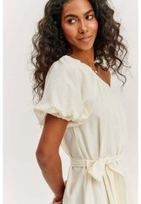 Biele, textúrované šaty s asymetrickým ramienkom, balónovými rukávmi a opaskom v páse. Mäkká tkanina s uvoľneným strihom.