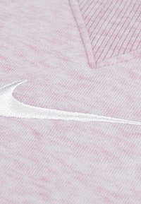 Light pink fabric with a textured finish, featuring a prominent white embroidered swoosh logo in the lower corner.