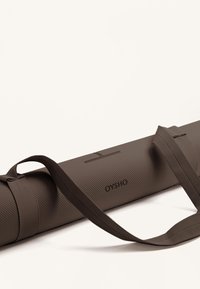 Jóga matrac táska textúrált barna anyagból. Pánttal rendelkezik a hordozáshoz, diszkrét márkás logóval. Henger alakú és tartós kialakítás.