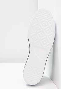 Bílá gumová podrážka sportovní obuvi s texturovaným geometrickým vzorem, s černým akcentem podél okraje a značkováním poblíž části paty.