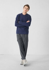 Sudadera azul marino con cuello redondo y puños acanalados, combinada con pantalones cargo gris oscuro con bolsillos laterales. Zapatillas deportivas gris claras.
