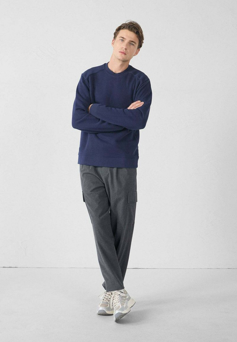 Sudadera azul marino con cuello redondo y puños acanalados, combinada con pantalones cargo gris oscuro con bolsillos laterales. Zapatillas deportivas gris claras.