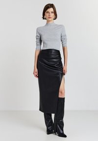 Grauer gerippter Pullover mit langen Ärmeln, kombiniert mit einem schwarzen Lederrock mit Seitenschlitz und kniehohen schwarzen Stiefeln.
