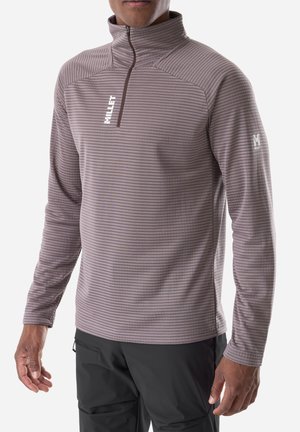 Man wearing a brown striped long-sleeve pullover with a front zipper and black pants, standing against a white background.