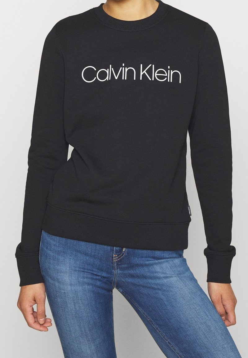 Felpa nera con colletto a girocollo, maniche lunghe e logo bianco "Calvin Klein" ben visibile sul davanti. Texture liscia.