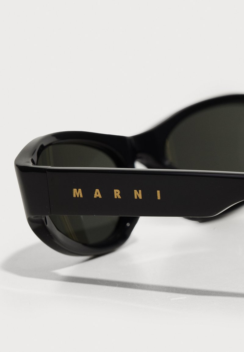 Sorte solbriller med mørke linser, der har en dristig geometrisk ramme og et guld "MARNI" logo på siden. Glat plastmateriale.