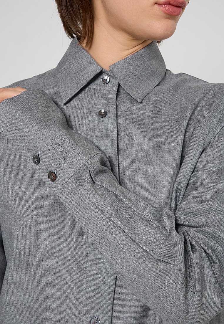 Graues Hemd mit strukturiertem Kragen, langen Ärmeln mit knöpfbaren Manschetten und einem strukturierten Stoff. Dezentes Branding am Ärmel.