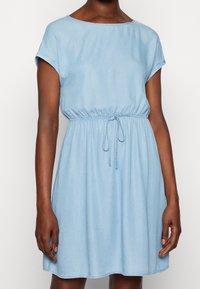 Světle modré džínové šaty s krátkými ohrnutými rukávy, elastickým pasem a nastavitelným šňůrkovým páskem. Hladká textura, délka ke kolenům.