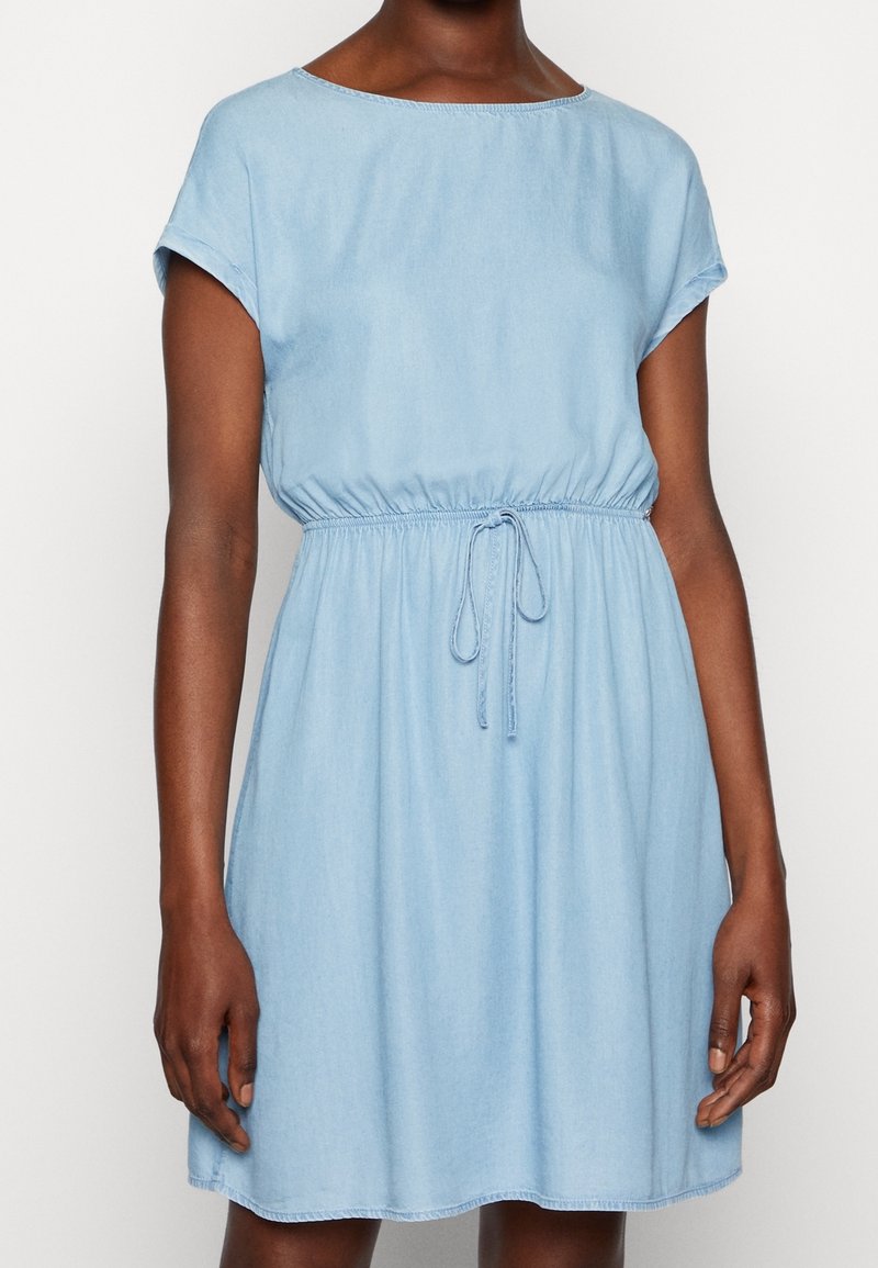 Světle modré džínové šaty s krátkými ohrnutými rukávy, elastickým pasem a nastavitelným šňůrkovým páskem. Hladká textura, délka ke kolenům.