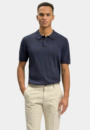 Mørkeblå kortærmet polo-shirt med ribbet tekstur og klassisk krave, parret med lys beige bukser. Enkel knapdetalje ved halsudskæringen.