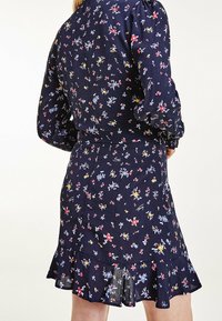 Abito navy con stampa floreale in rosso, giallo e blu. Maniche lunghe a sbuffo, vita aderente, orlo arricciato e tessuto strutturato.