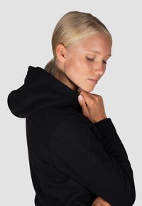 Schwarzer Kapuzenpullover mit weicher Textur. Besitzt einen lockeren Sitz und sichtbare Nähte an der Kapuze und den Bündchen.